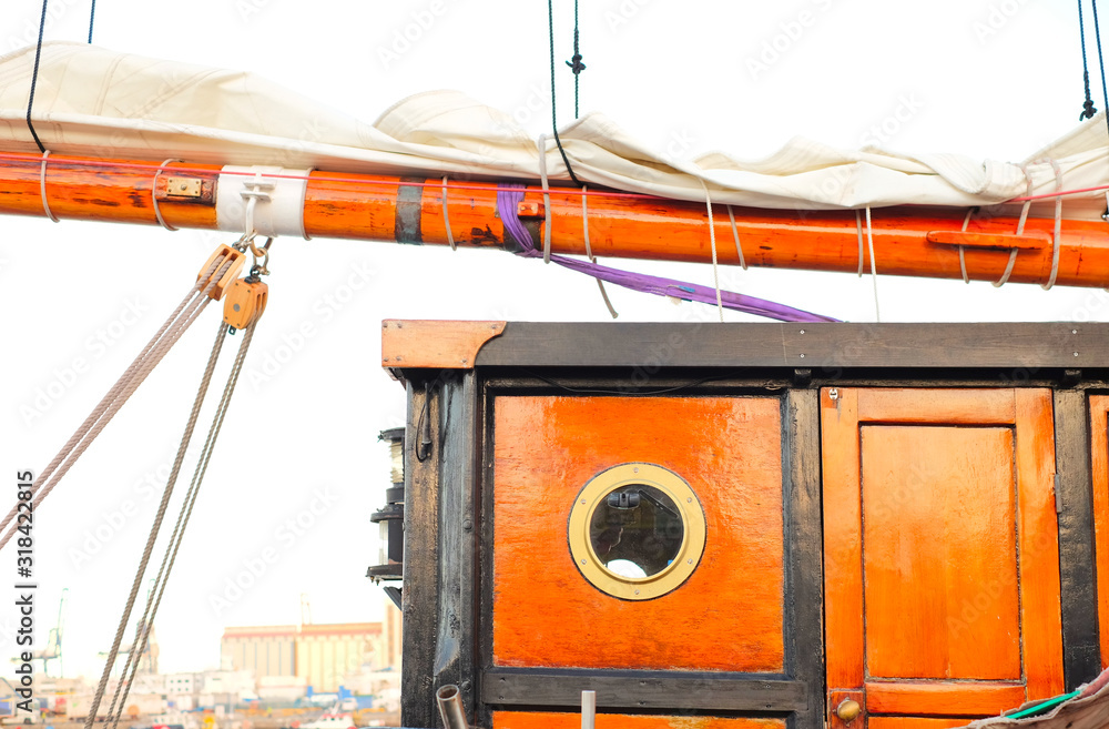 Naklejka premium Detail of a classic sailing tall ship, doghouse cabin with a round porthole, a sail flaked on a wooden boom and a sheet tackle.