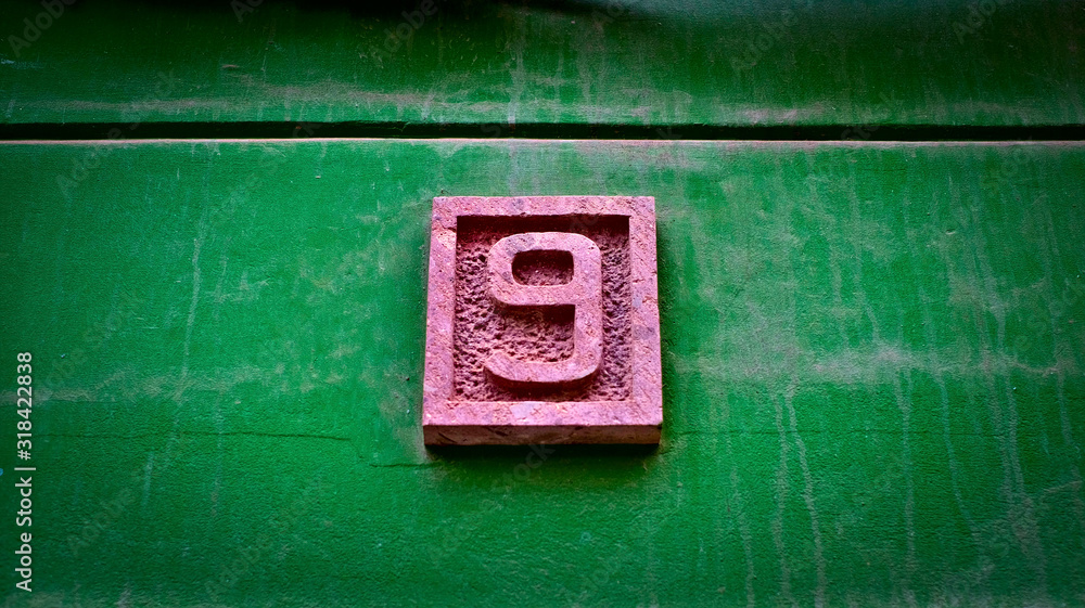 Number 9, nine, sandstone relief digit on a vivid green wall background. Number 9, nine, sandstone relief digit on a vivid green wall background.