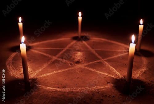 White pentagram symbol on concrete ground. Illuminated with candles. Dark background. Scary, mystical occultism  photo
