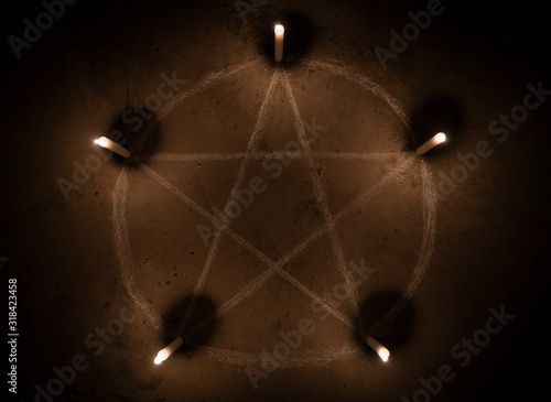 White pentagram symbol on concrete ground. Illuminated with candles. Dark background. Scary, mystical occultism 