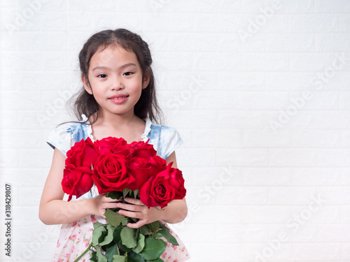 Happy Asian little cute girl standing and holding red rose bouquet over white bricks wall background. 