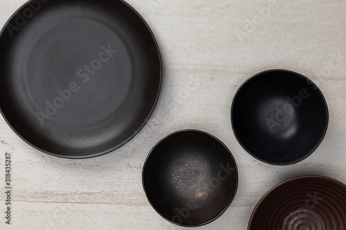Group of empty blank black ceramic round bowls and plates on white stone blackground, Top view of traditional handcrafted kitchenware concept