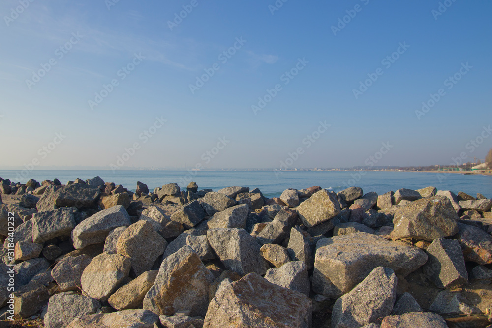 Many large stones on the seashore against the background of water and the city in the distance. Many large stones on the seashore against the background of water and the city in the distance.