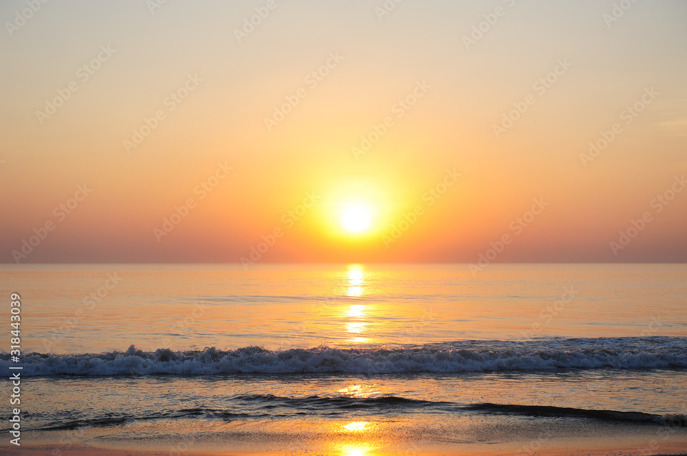 Stunning view of the sea in the rays of setting sun, reddish sunlight reflected in the water. Beautiful sunset over the ocean, deserted beach, copy space.