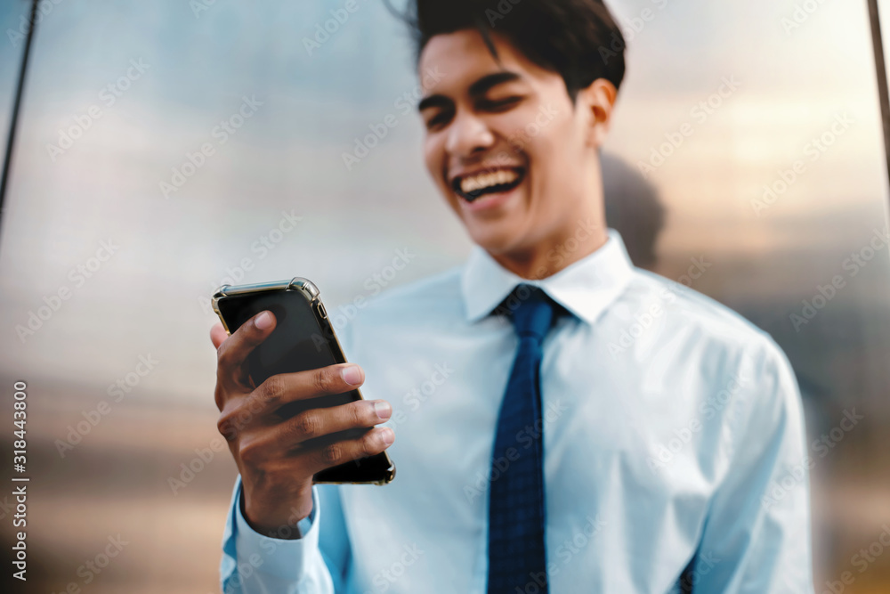 Blurred of a Happy Young Businessman Using Mobile Phone in the Urban City. Lifestyle of Modern People. Front View. Standing by the Wall. Selective Focus on Smartphone Blurred of a Happy Young Businessman Using Mobile Phone in the Urban City. Lifestyle of Modern People. Front View. Standing by the Wall. Selective Focus on Smartphone