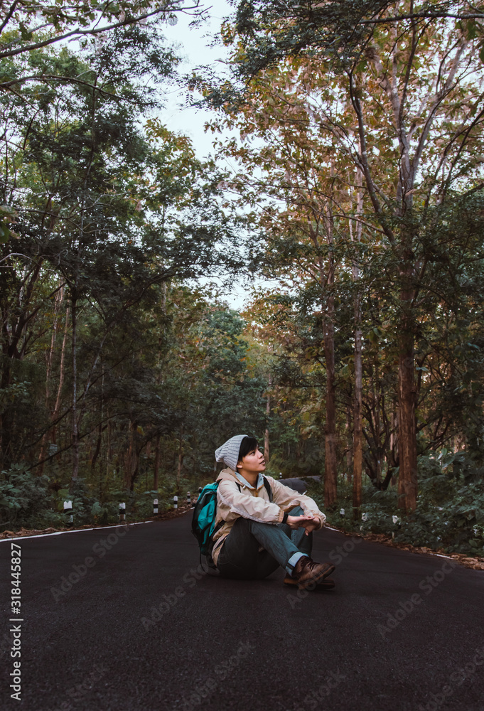 Asian young man in boots on sitting the road in mountains with enjoying their alone forest outdoor active lifestyle travel adventure, people hiking vacations in Thailand.
