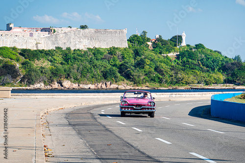 Pink old cabriolet rides along Malecon embankment against the background of the old Fort. el Morro lighhouse photo