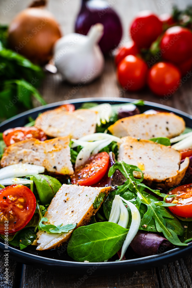 Caesar salad - barbecue chicken breast and vegetables on wooden table Caesar salad - barbecue chicken breast and vegetables on wooden table