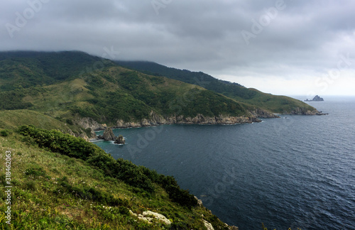 Beautiful seascape - green hills, sea, island on the horizon under a cloudy sky.