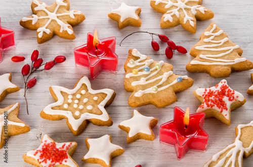 Beautiful homemade Christmas cookies with white icing, red candles and berries on wooden background, close-up