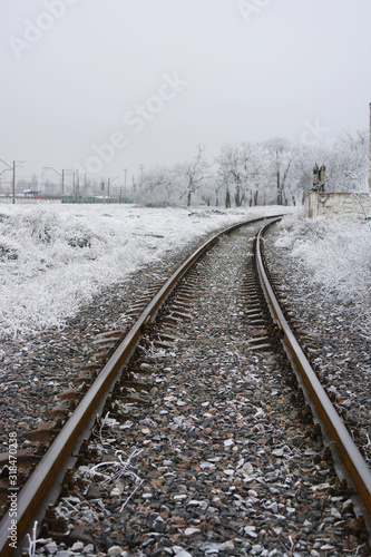 A railroad line running along a white cement fence that is covered with fluffy white snow in winter.