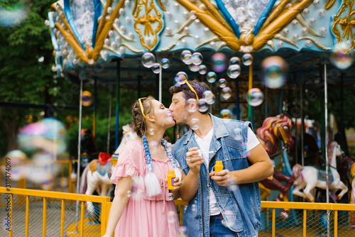 A beautiful bright cheerful romantic couple in love enjoy soap bubbles in an amusement Park and kiss