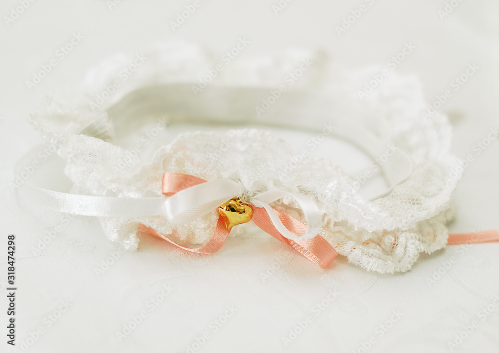 White lace garter for the bride with a coral satin ribbon and a gold heart on a white background White lace garter for the bride with a coral satin ribbon and a gold heart on a white background