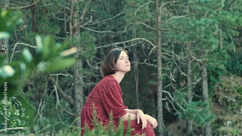 Young attractive woman in red dress sitting and thinkin in green forest during sunset time in Esperanza, Tenerife, Canary, Spain photo