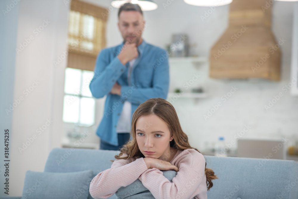 Pensive father standing behind seated sad daughter. Pensive father standing behind seated sad daughter.