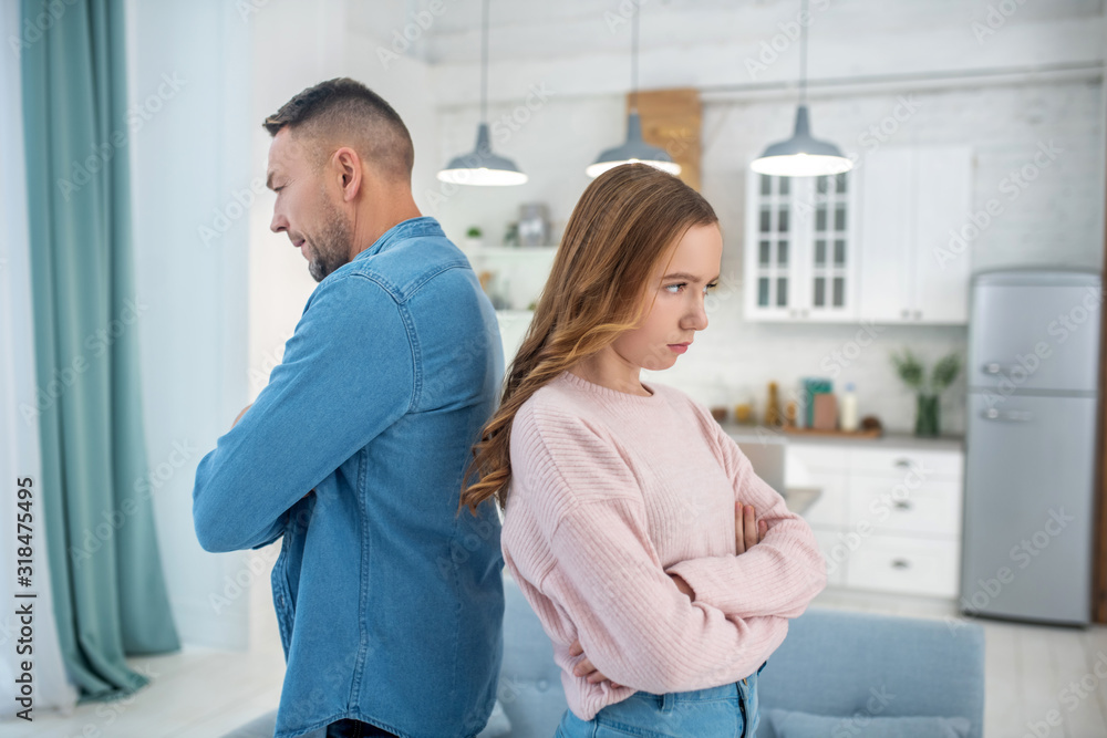 Father and daughter standing back to back, arms crossed. Father and daughter standing back to back, arms crossed.