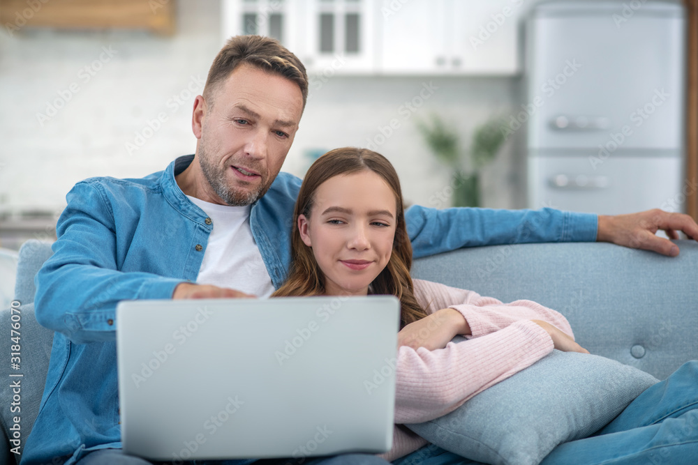 Father pointing to laptop screen and daughter sitting on couch. Father pointing to laptop screen and daughter sitting on couch.