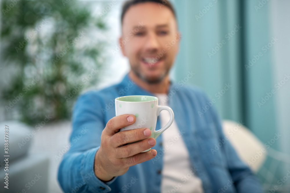 Cup of tea in the man's outstretched hand. Cup of tea in the man's outstretched hand.