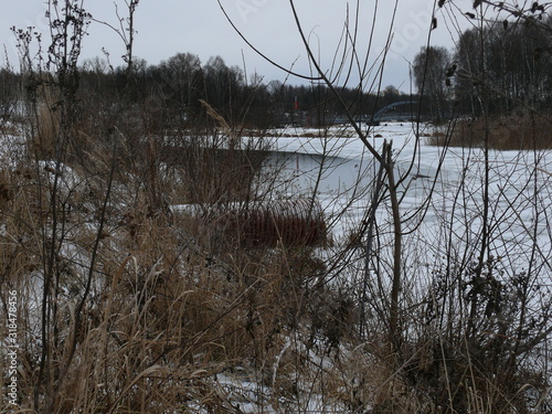 winter river with a bank covered with dry grass and a sewage pipe into the river for its pollution.