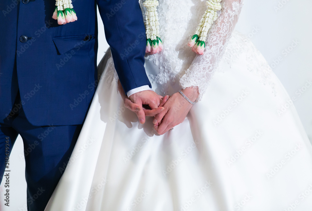 Bride and Groom in formal costumes with flower garlands, looking nervous, holding hands on the stage in traditional Thai wedding reception ceremony. Life Event, Marriage, Moment and Emotion concept Bride and Groom in formal costumes with flower garlands, looking nervous, holding hands on the stage in traditional Thai wedding reception ceremony. Life Event, Marriage, Moment and Emotion concept