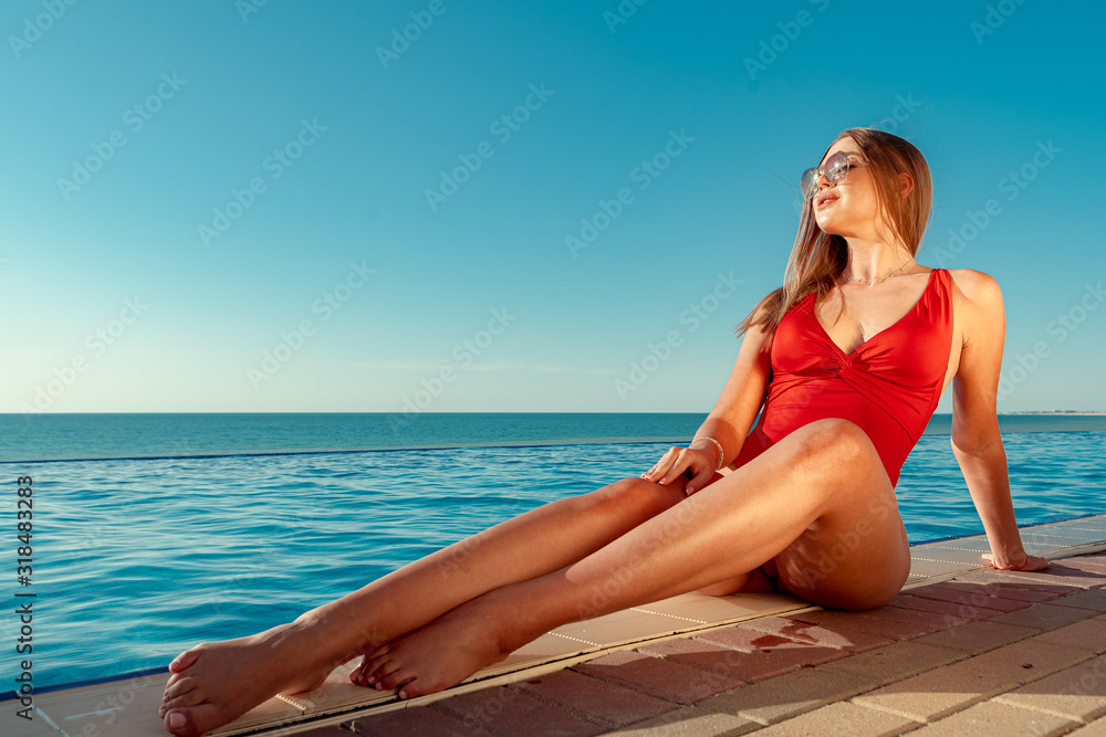 Fashionable woman in red bikini sitting near the pool