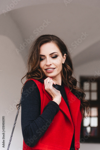 Obraz na płótnie Outdoor portrait of a stylish young girl on the street of an old city in black clothes and a long red vest. A model poses on the street of a European city w salonie