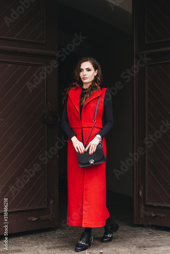 Obraz na płótnie Outdoor portrait of a stylish young girl on the street of an old city in black clothes and a long red vest. A model poses on the street of a European city w salonie