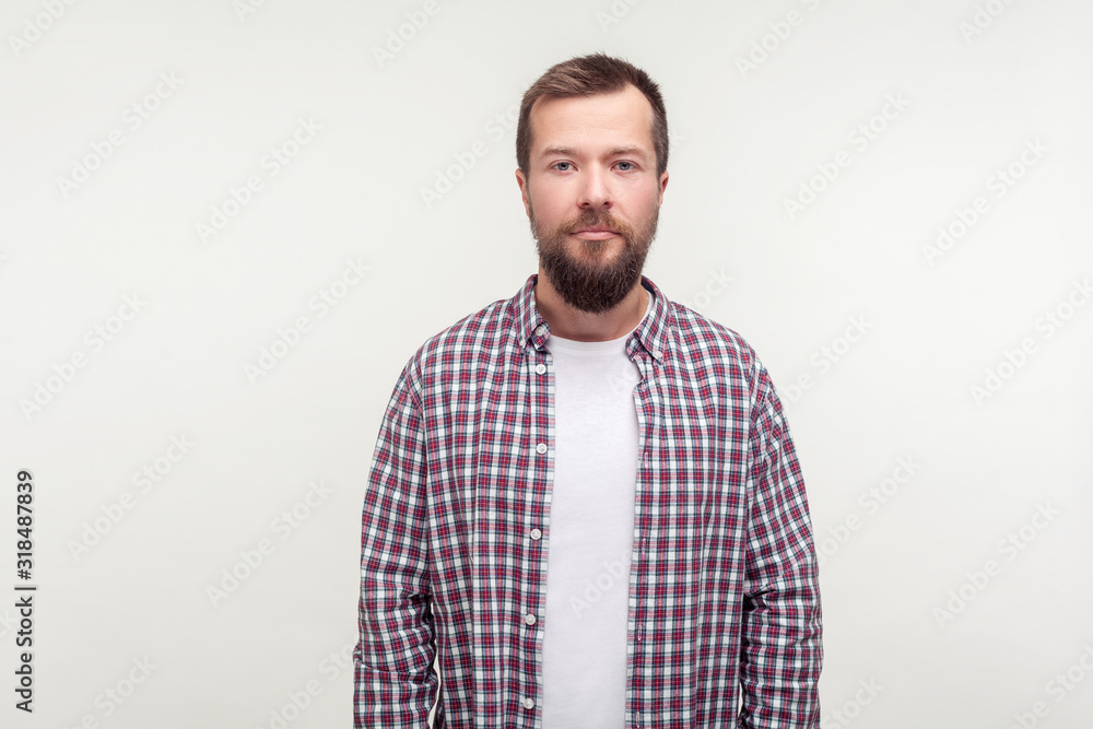 Portrait of serious bearded young man in plaid shirt standing looking at camera with calm confident attentive expression, worker or employee in casual outfit. studio shot isolated on white background Portrait of serious bearded young man in plaid shirt standing looking at camera with calm confident attentive expression, worker or employee in casual outfit. studio shot isolated on white background