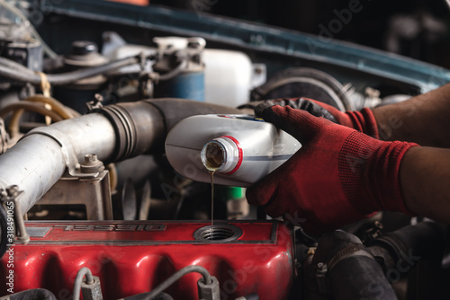 Hands of auto repair mechanic filling lubricant oil in engine of car during service - Vehicle maintenance technician carrying out annual servicing inspection - Garage, industry and mechanical concept