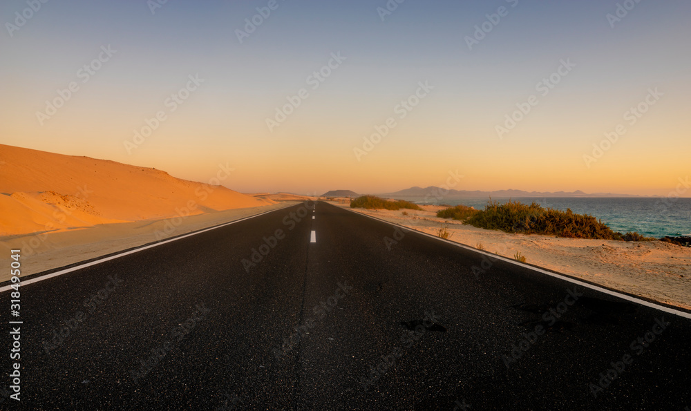 asphalt road running across the desert on the ocean shore at sunrise