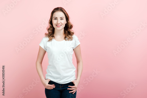 Young  beautiful woman in white t-shirt and jeans posing on pink wall background
