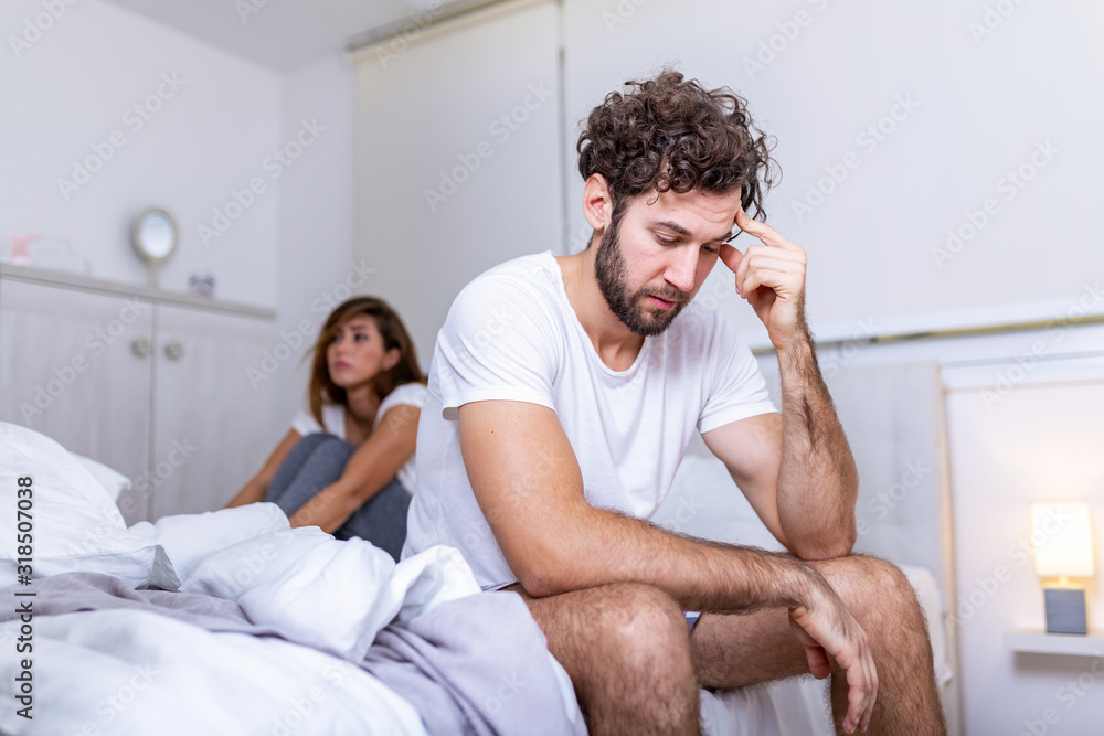Beautiful girl and a frustrated man sitting in bed and not looking at each other. Upset couple ignoring each other. Worried man in tension at bed. Young couple angry with each other after a fight.