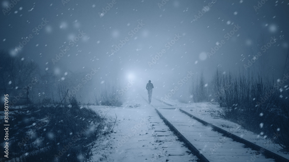 Alone man walks along a railway track in a heavy snowfall to meet a train . Misty mystical road. Film toning