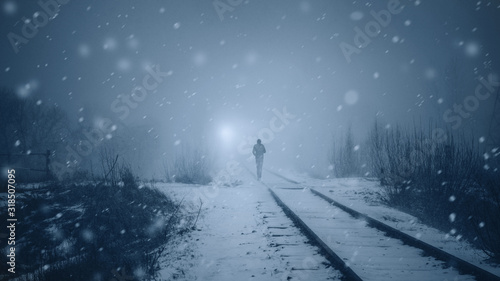 Alone man walks along a railway track in a heavy snowfall to meet a train . Misty mystical road. Film toning