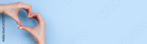 Female hands show a heart symbol on a light blue background. Place for text, copy space, banner format.