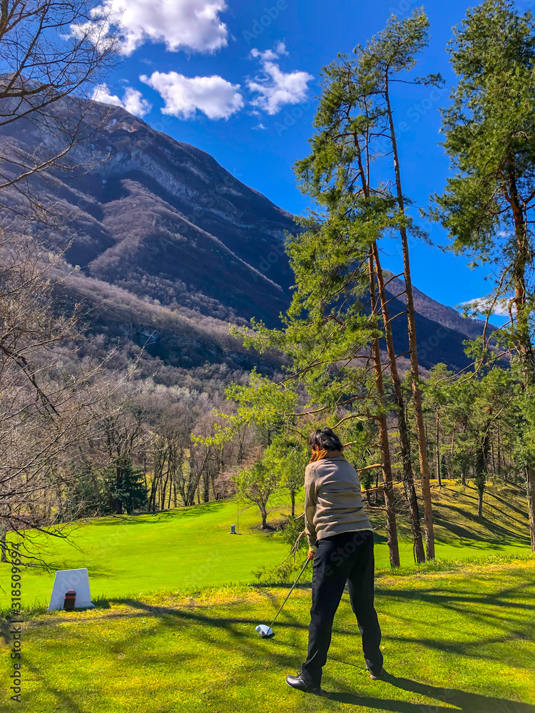 Golfer Teeing Off with Driver and with Mountain View in Italy.
