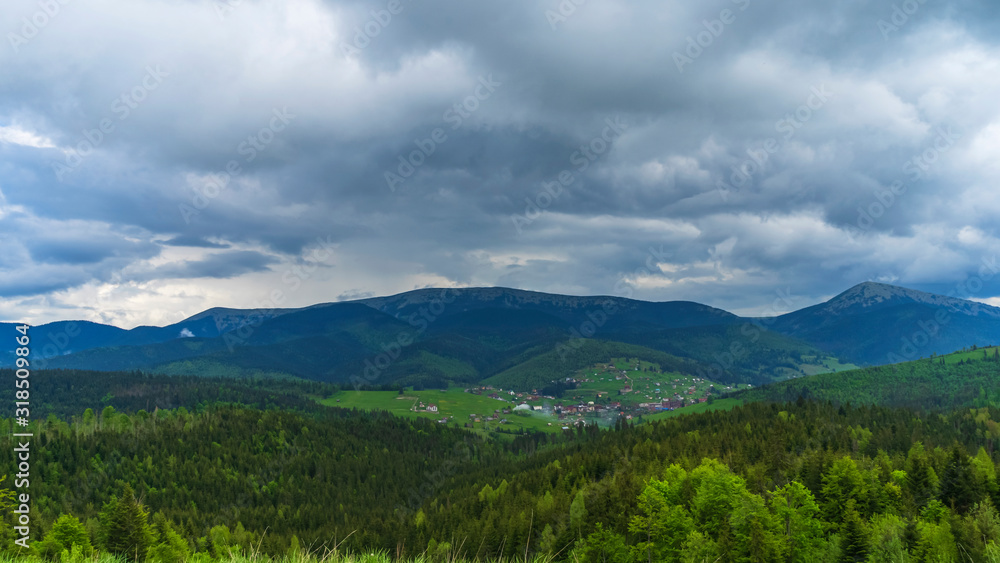 Magnificent panoramic view the coniferous forest on the mighty Carpathians Mountains and beautiful sky and village background. Beauty of wild virgin Ukrainian nature. Peacefulness