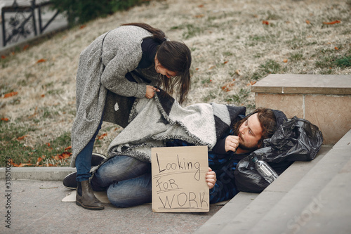 Homeless in a city. Man asking for food. Man with a tablet. Girl helping a homeless