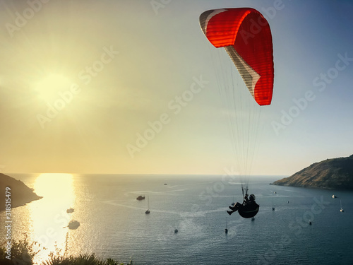 A man is engaged in paragliding. Red Parachute in the blue sky against the background of yachts, sea and islands.