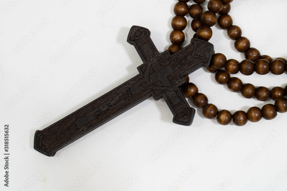 rosary beads with cross made of black wood on a white background, selected focus on christ, narrow depth of field.