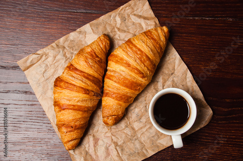 Delicious croissants and ristretto coffee in a white cup on vintage crumpled craft paper, on dark wooden tabletop