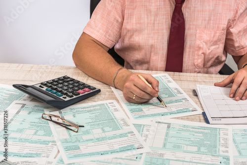 Man filling 1040 tax form at workplace. Performing tax calculations. Close up.
