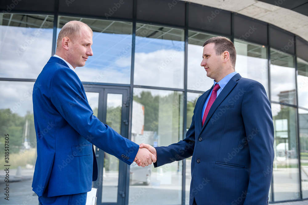 Business partners handshaking before big building outdoors Business partners handshaking before big building outdoors