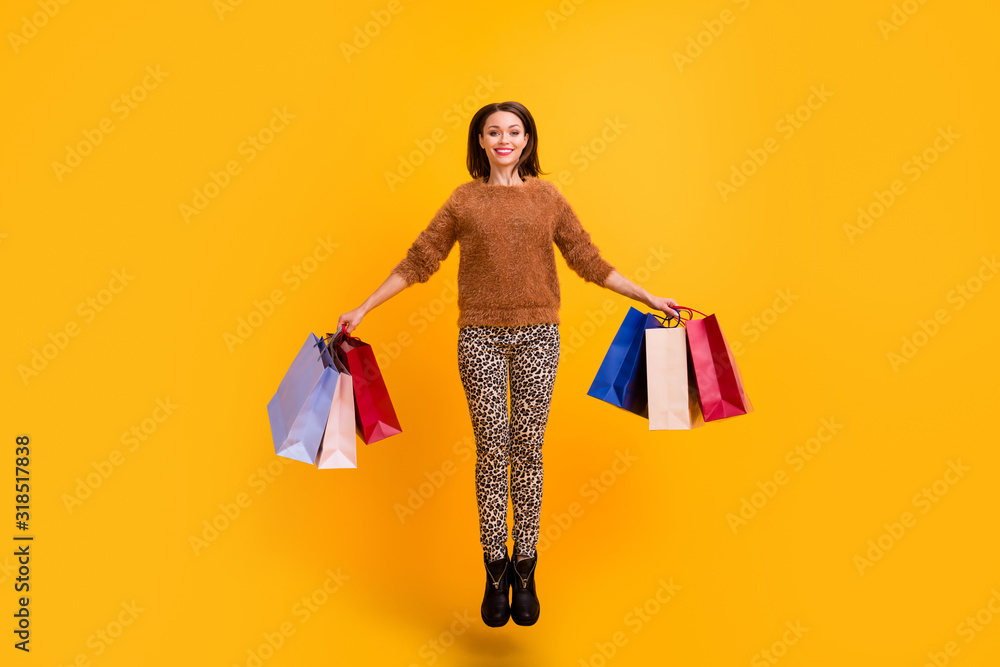 Fototapeta premium Full body photo of pretty overjoyed lady jump high carry packs addicted shopaholic wear casual fluffy sweater leopard trousers boots isolated yellow color background