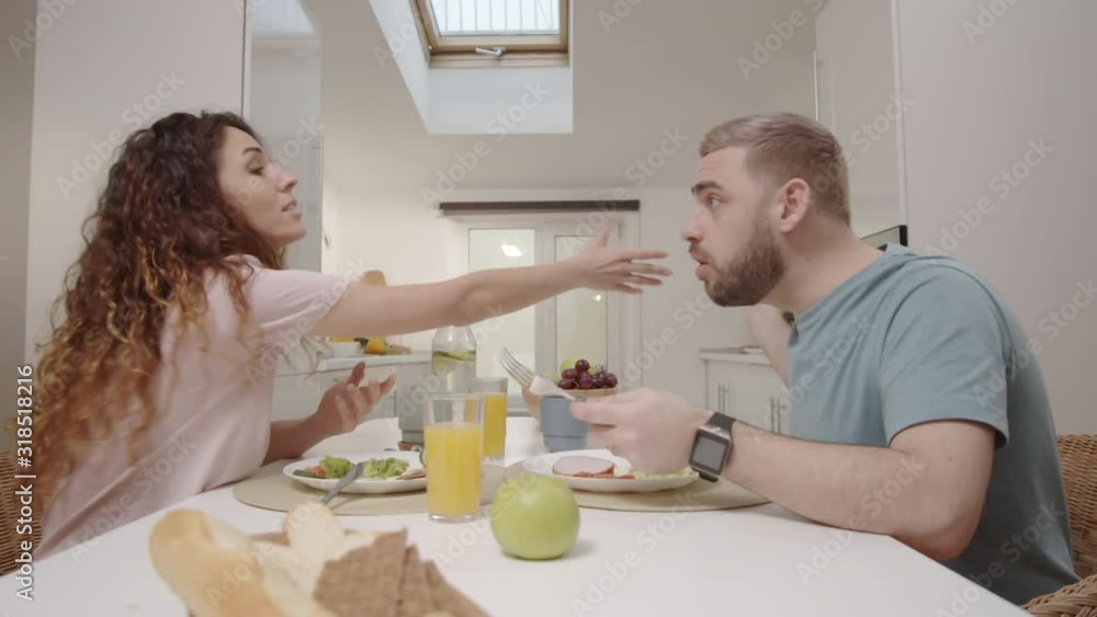 Medium shot of young Caucasian woman using smartphone during dinner with husband at home, annoyed man confiscating it, woman demanding it back and trying to fight, and man throwing it away Medium shot of young Caucasian woman using smartphone during dinner with husband at home, annoyed man confiscating it, woman demanding it back and trying to fight, and man throwing it away