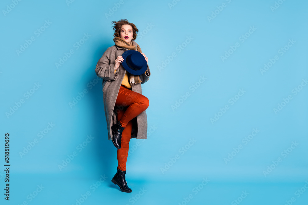 Full length profile photo of amazing lady jumping high up holding stylish retro cap wear casual long grey coat scarf trousers shoes isolated blue color background Full length profile photo of amazing lady jumping high up holding stylish retro cap wear casual long grey coat scarf trousers shoes isolated blue color background