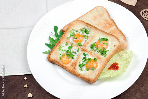 Scrambled fried eggs and bread in the shape of a heart with hot toasts and fresh vegetables served on a wooden table. Romantic breakfast on Valentine's Day or Mother's Day. Top view, closeup