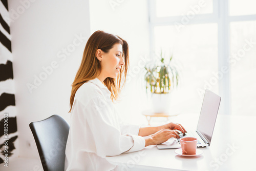 Happy beautiful woman in white shirt working on a laptop.