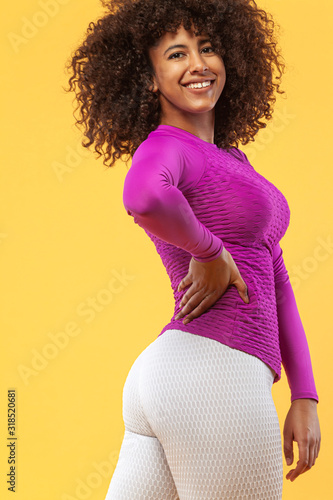 Smiling strong athletic woman with black skin and curly hair, doing exercise on yellow background wearing sportswear. Fitness and sport motivation. photo