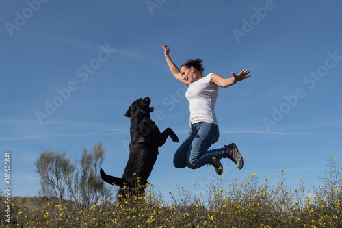 Labrador dog with middle-aged woman jumping together with joy in nature.